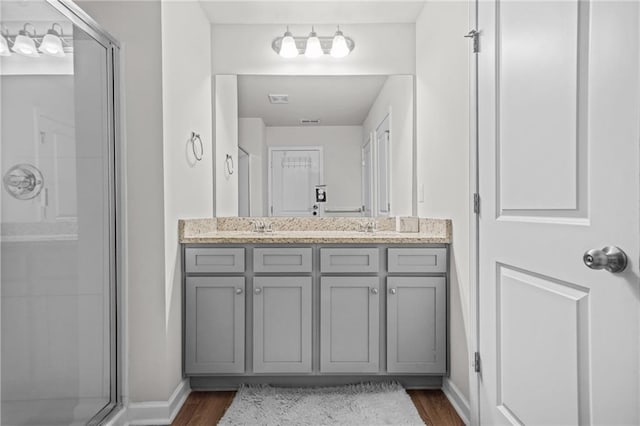 full bathroom featuring a sink, a stall shower, double vanity, baseboards, and wood finished floors