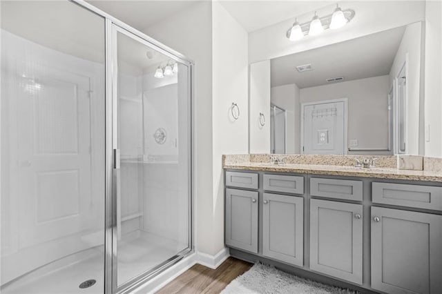 full bathroom featuring a sink, double vanity, visible vents, wood finished floors, and a shower stall