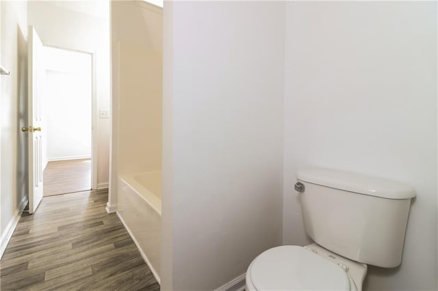 bathroom featuring a tub to relax in, baseboards, toilet, and wood finished floors