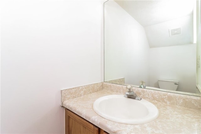 bathroom with vanity, visible vents, vaulted ceiling, and toilet