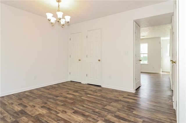 empty room featuring dark wood-style flooring, baseboards, and a notable chandelier