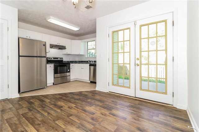 kitchen featuring white cabinetry, dark countertops, under cabinet range hood, appliances with stainless steel finishes, and wood finished floors