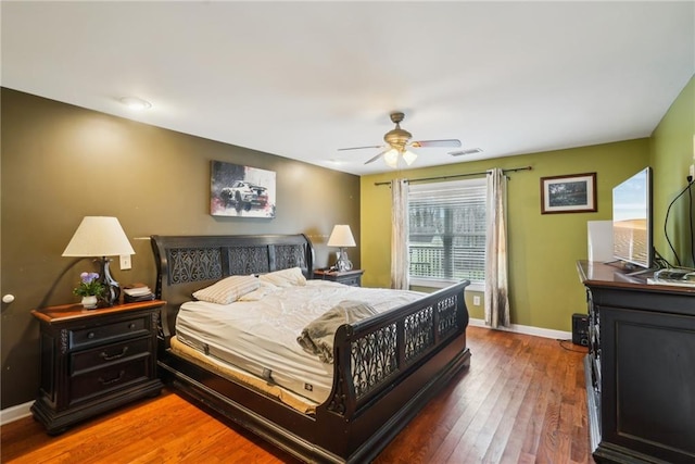 bedroom with a ceiling fan, visible vents, baseboards, and wood finished floors