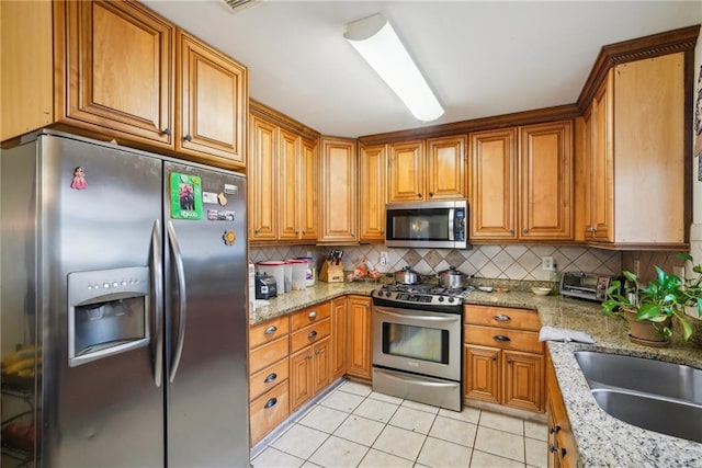 kitchen with light stone counters, light tile patterned floors, tasteful backsplash, appliances with stainless steel finishes, and brown cabinetry