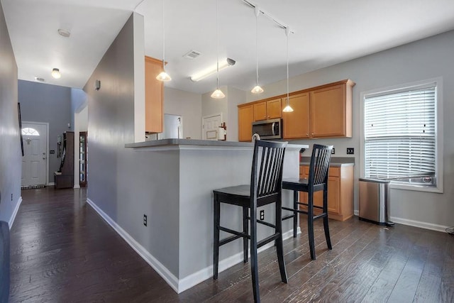 kitchen with stainless steel microwave, a breakfast bar, dark wood-type flooring, and baseboards