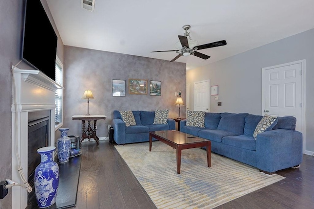 living room featuring a ceiling fan, wood finished floors, visible vents, and a fireplace with raised hearth