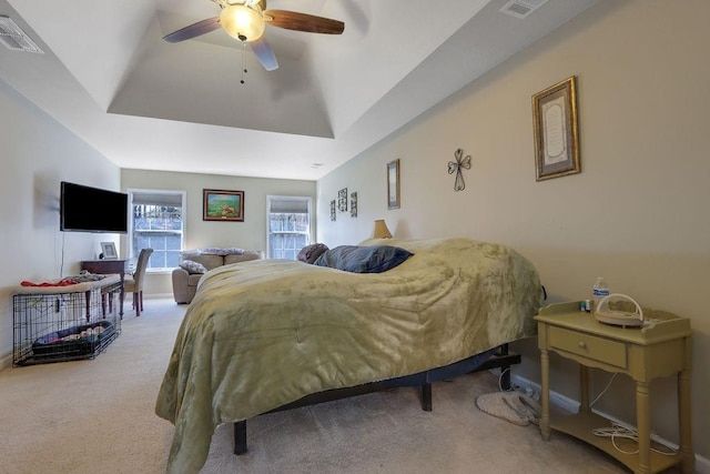 carpeted bedroom featuring visible vents, a raised ceiling, and a ceiling fan