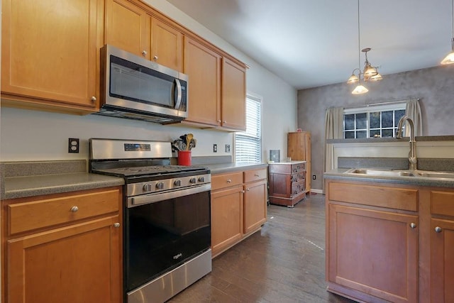 kitchen featuring dark countertops, a sink, hanging light fixtures, stainless steel appliances, and dark wood-style flooring