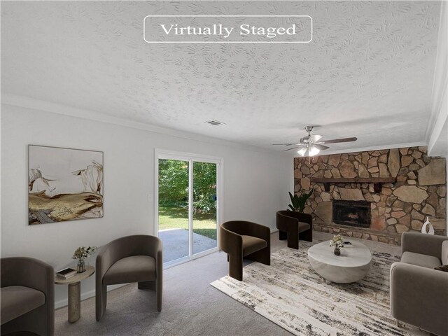 carpeted living room featuring ceiling fan, a stone fireplace, ornamental molding, and a textured ceiling