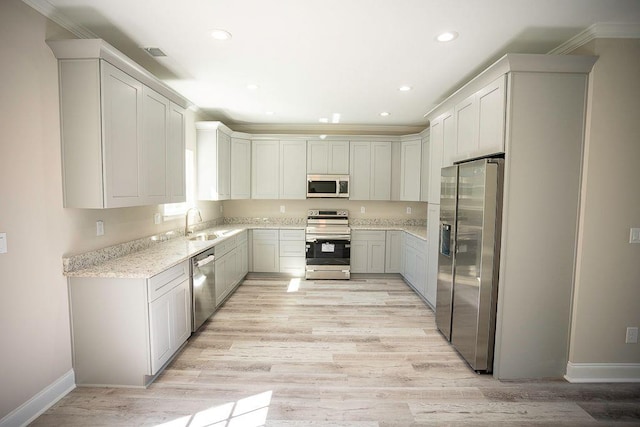 kitchen with appliances with stainless steel finishes, white cabinetry, ornamental molding, light stone counters, and light wood-type flooring