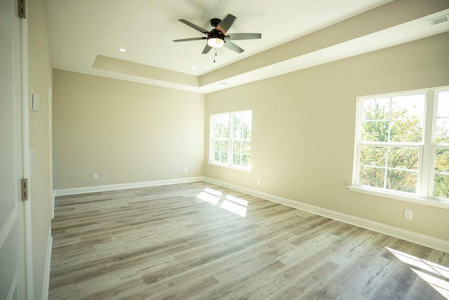 empty room featuring light hardwood / wood-style flooring, ceiling fan, and a tray ceiling