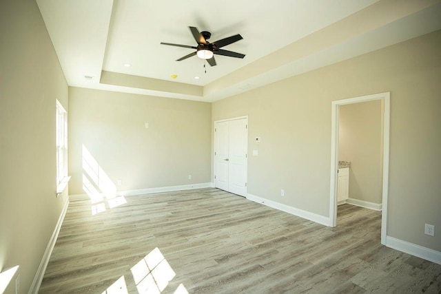 unfurnished bedroom featuring a closet, light hardwood / wood-style flooring, ceiling fan, and a tray ceiling