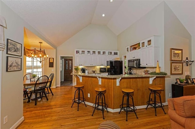 kitchen featuring a breakfast bar area, white cabinets, light hardwood / wood-style floors, light stone countertops, and black fridge