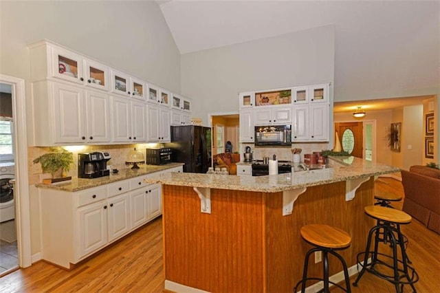 kitchen featuring light hardwood / wood-style floors, white cabinetry, black appliances, and a kitchen breakfast bar