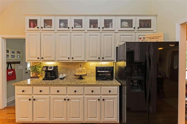 kitchen with light hardwood / wood-style flooring, decorative backsplash, light stone counters, and black refrigerator with ice dispenser