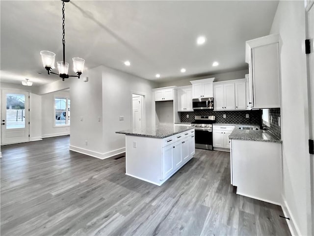 kitchen featuring white cabinets, a kitchen island, stone counters, stainless steel appliances, and backsplash