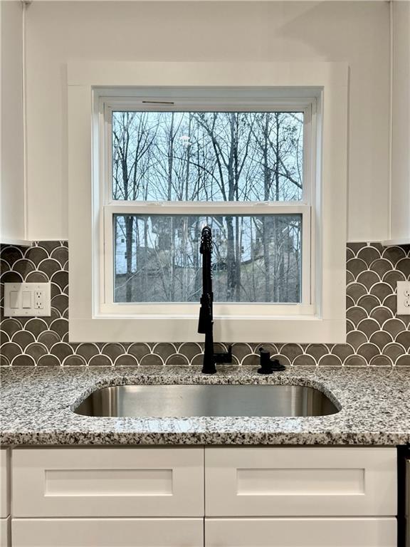 room details featuring tasteful backsplash, white cabinetry, light stone countertops, and sink