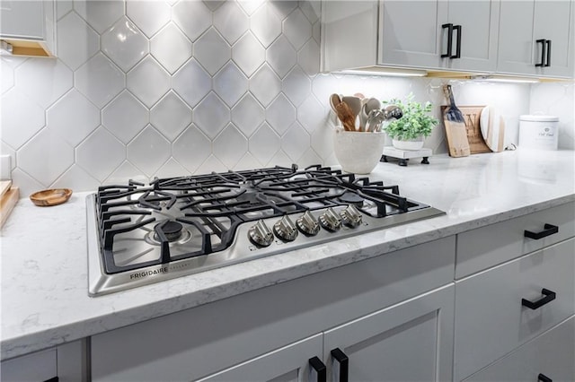 interior details featuring white cabinets, decorative backsplash, light stone counters, and stainless steel gas cooktop