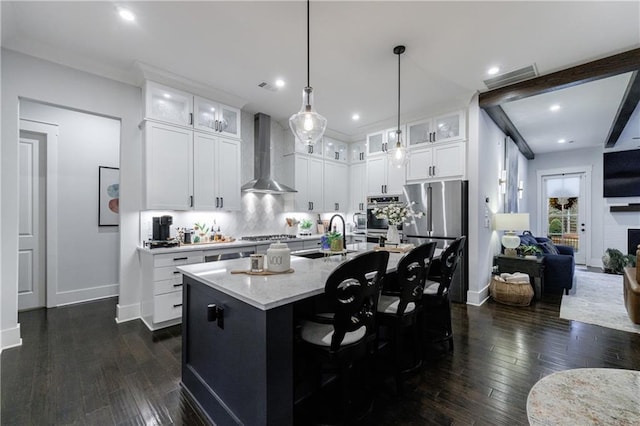 kitchen with dark hardwood / wood-style flooring, wall chimney exhaust hood, stainless steel appliances, white cabinets, and an island with sink