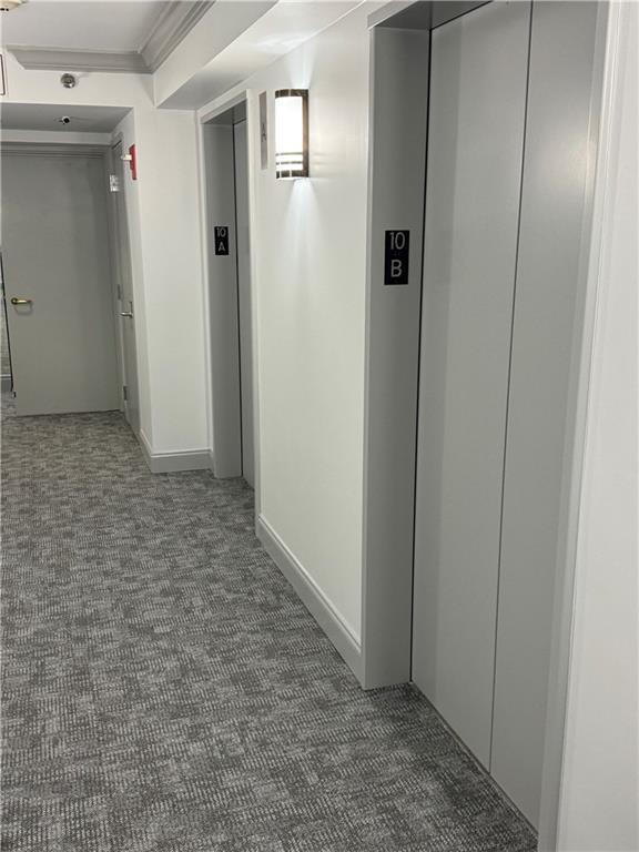 corridor featuring elevator, dark colored carpet, and ornamental molding