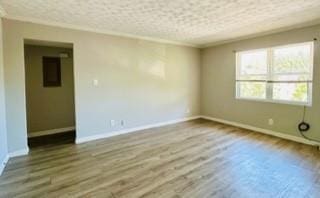 empty room with a textured ceiling, hardwood / wood-style floors, and crown molding