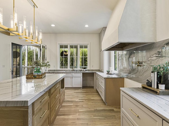 kitchen with backsplash, hanging light fixtures, light stone counters, light hardwood / wood-style floors, and custom range hood