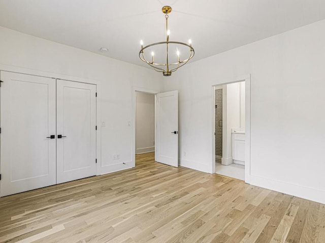 unfurnished bedroom featuring ensuite bathroom, a closet, a notable chandelier, and light hardwood / wood-style flooring