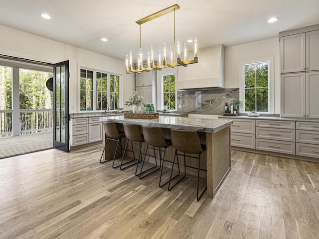 kitchen with gray cabinetry, light stone counters, a kitchen breakfast bar, custom range hood, and a kitchen island