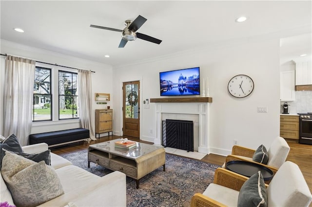 living area with baseboards, a fireplace with flush hearth, ornamental molding, recessed lighting, and wood finished floors