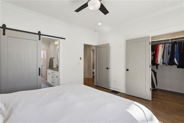 bedroom with visible vents, ornamental molding, wood finished floors, a barn door, and a spacious closet