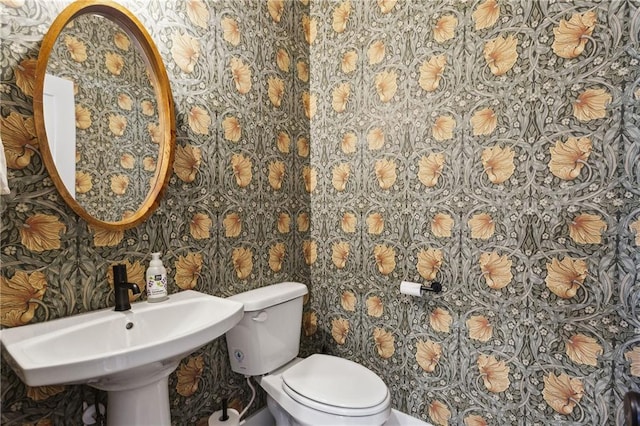 half bathroom featuring wallpapered walls, toilet, and a sink