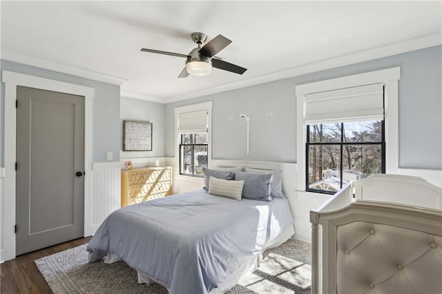 bedroom featuring multiple windows, dark wood-style floors, a wainscoted wall, and ornamental molding