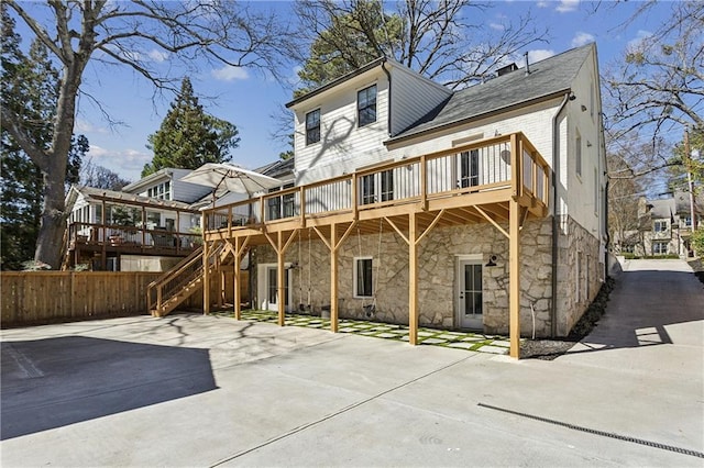 rear view of house featuring stone siding, stairway, a wooden deck, and fence