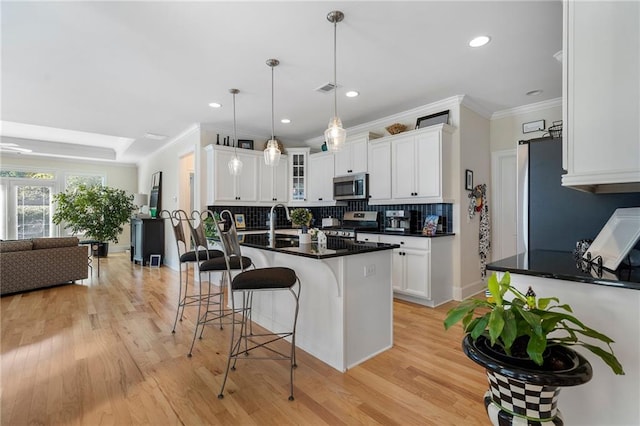 kitchen featuring a kitchen island with sink, light hardwood / wood-style floors, a breakfast bar, stainless steel appliances, and white cabinetry