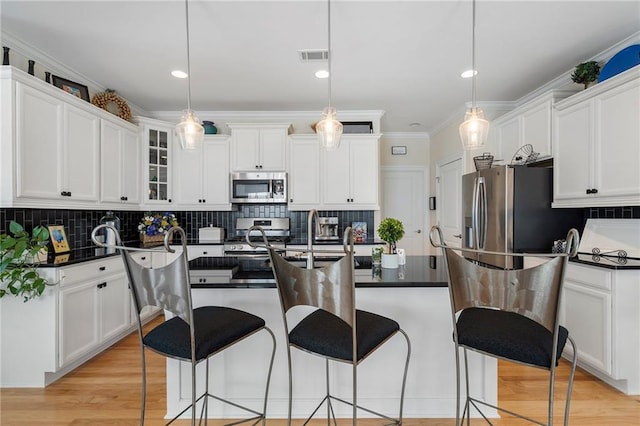 kitchen featuring crown molding, decorative light fixtures, an island with sink, appliances with stainless steel finishes, and white cabinets