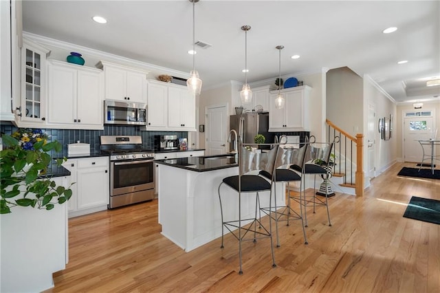 kitchen with white cabinetry, stainless steel appliances, sink, hanging light fixtures, and light hardwood / wood-style floors