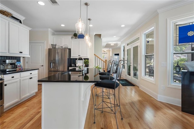 kitchen with stainless steel fridge, light hardwood / wood-style flooring, pendant lighting, a kitchen island with sink, and sink