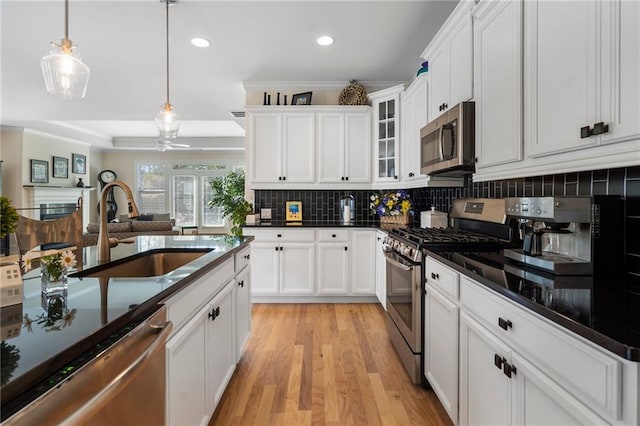 kitchen featuring light wood-type flooring, stainless steel appliances, sink, hanging light fixtures, and white cabinets