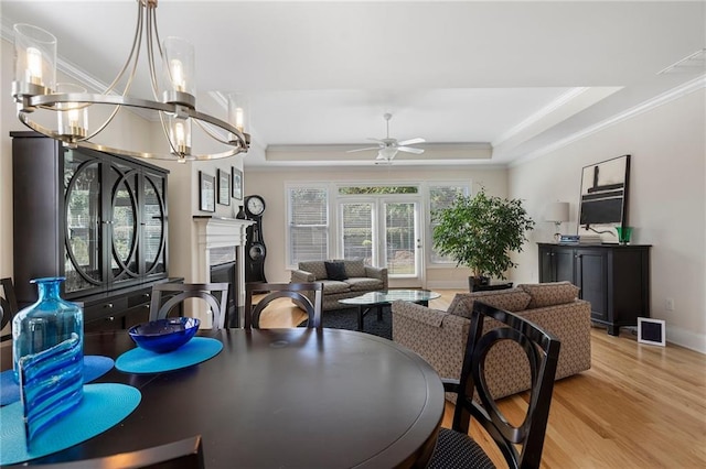 dining room featuring ceiling fan with notable chandelier, a raised ceiling, crown molding, and light wood-type flooring