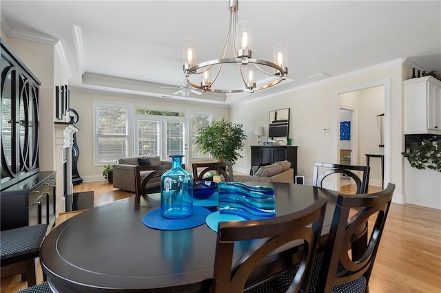 dining area with a raised ceiling, ornamental molding, ceiling fan with notable chandelier, and light wood-type flooring