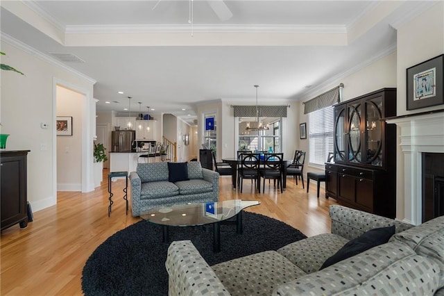 living room with crown molding, ceiling fan with notable chandelier, and light wood-type flooring