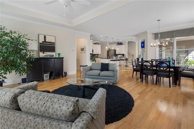 living room with ceiling fan with notable chandelier, crown molding, and light hardwood / wood-style flooring