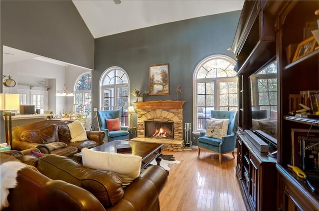 living room featuring a stone fireplace, high vaulted ceiling, light hardwood / wood-style floors, and a notable chandelier