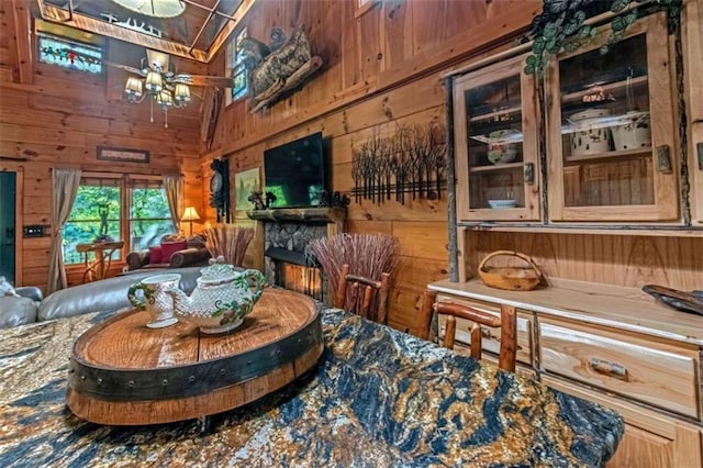 interior space with lofted ceiling, a stone fireplace, wooden walls, and a chandelier