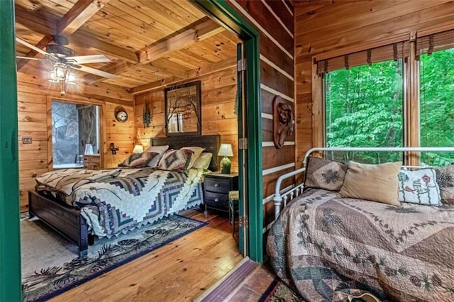 bedroom with ceiling fan, wood walls, wood-type flooring, and beam ceiling