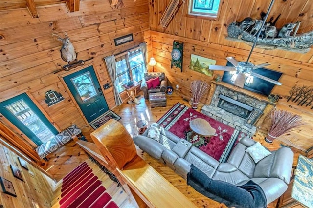 living room with hardwood / wood-style floors, ceiling fan, wood walls, and a stone fireplace