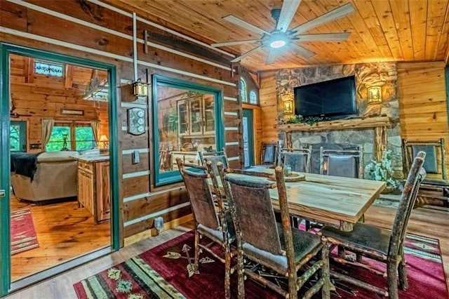 dining room with vaulted ceiling, wood walls, a fireplace, ceiling fan, and light wood-type flooring