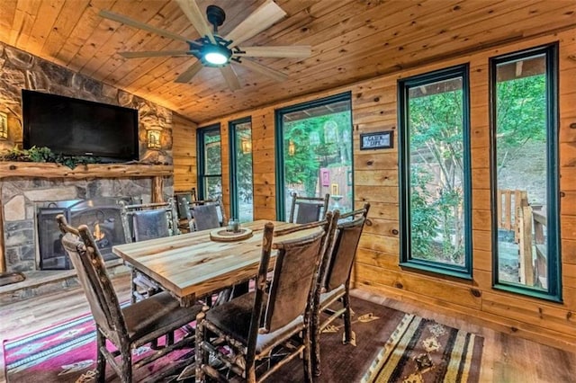 dining area with lofted ceiling, wooden walls, ceiling fan, and a stone fireplace