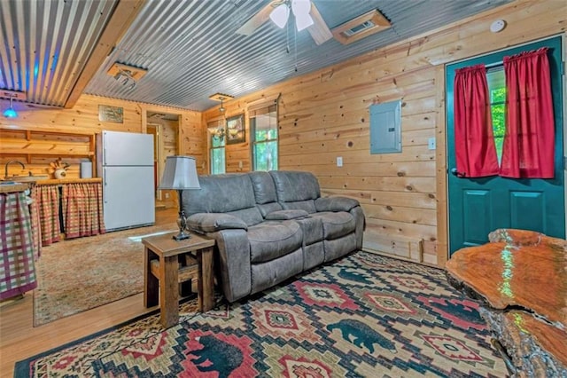 living room with wood-type flooring, sink, electric panel, ceiling fan, and wooden walls