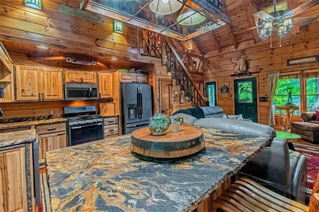 kitchen featuring wood walls, appliances with stainless steel finishes, stone counters, and vaulted ceiling with beams